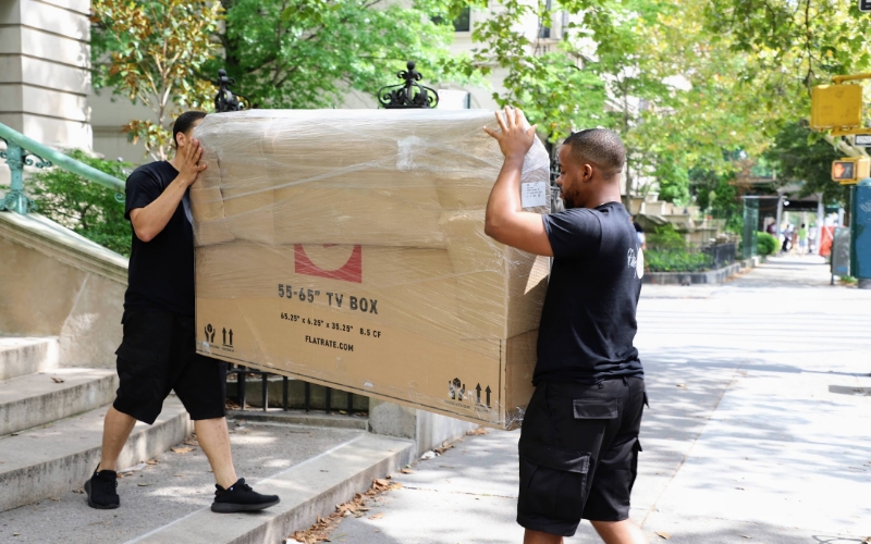 Two Flatrate movers moving a packed sofa