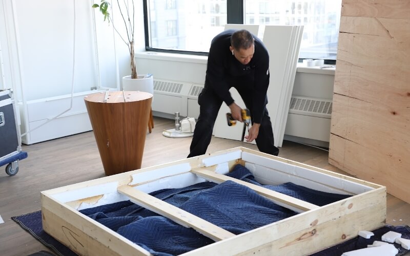 A Flatrate mover carefully packing an LED TV into a wooden crate for safe transportation