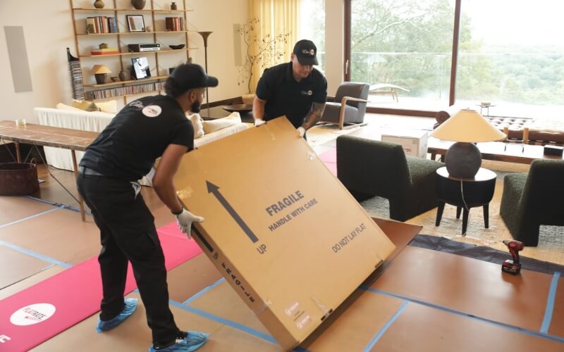 Two FlatRate movers carefully transporting a Flat TV box inside a home